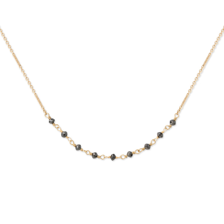 A delicate gold chain necklace featuring a curved line of small, faceted black beads separated by tiny gold links, displayed against a solid white background.