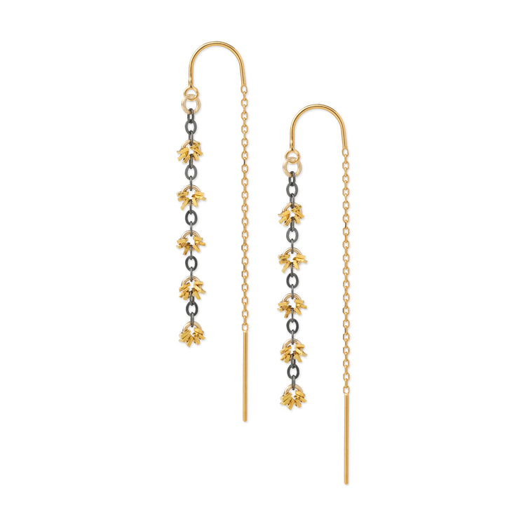 A pair of gold dangle earrings with floral motifs, featuring yellow-gold flower charms, dark metallic spacer rings, and a fine gold chain leading to a long straight drop.