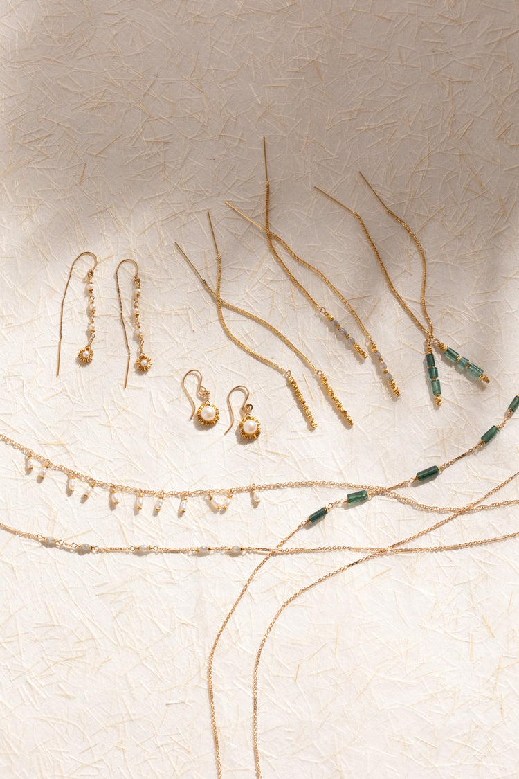Gold jewelry set including earrings and necklaces on a textured beige background
