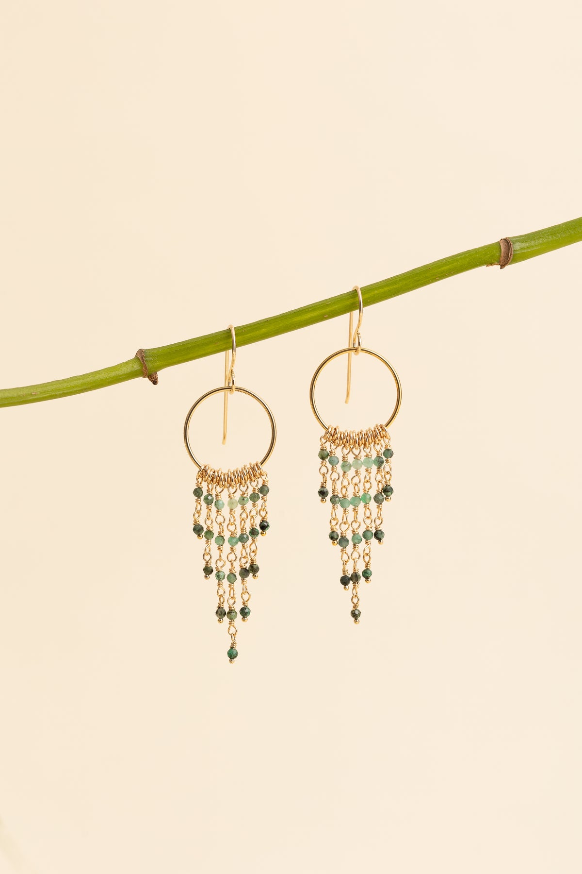 Emerald fringe earrings hanging on a branch
