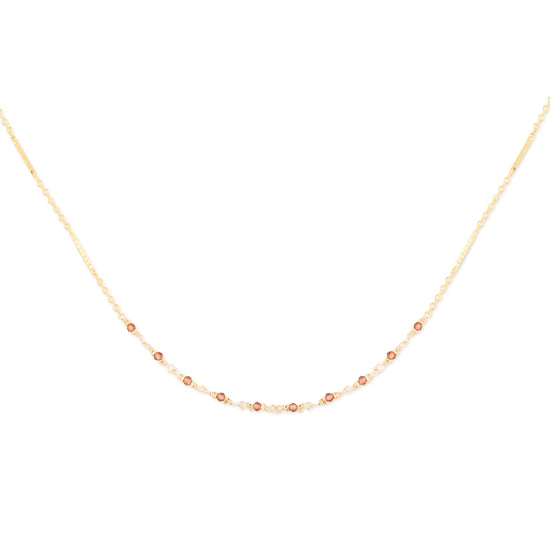 Delicate gold necklace with small garnet beads on a white background
