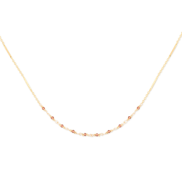 Delicate gold necklace with small garnet beads on a white background