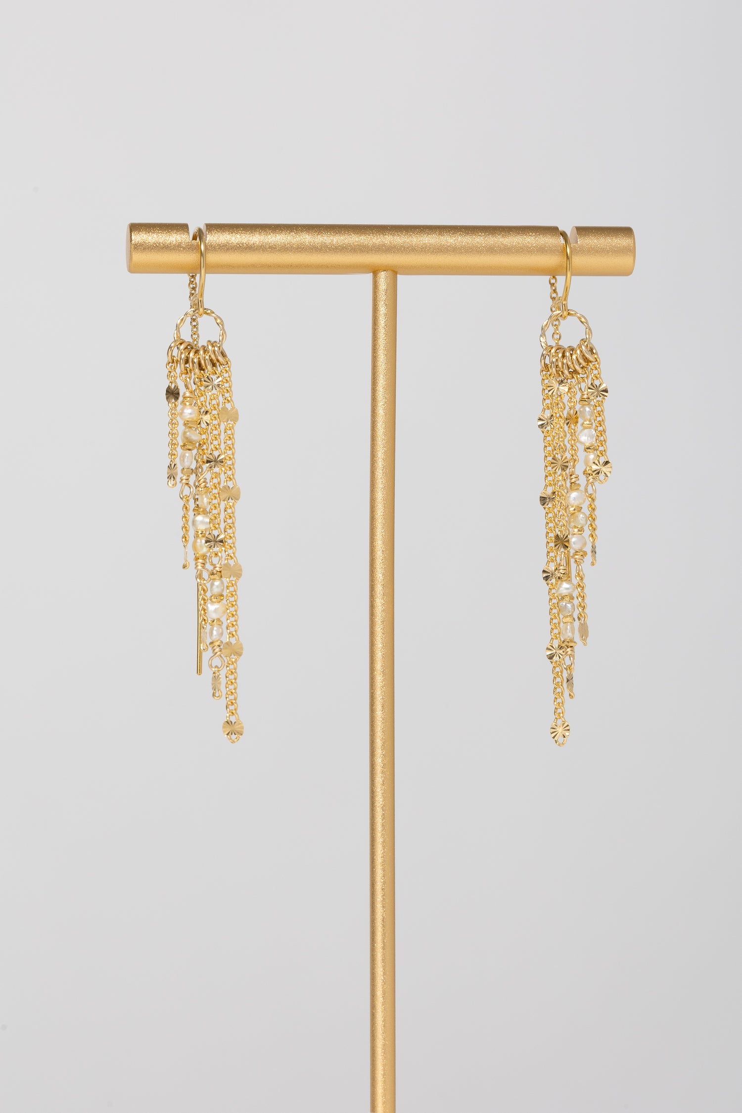 Slanted gold fringe threader earrings with pearl accents on a gold stand with light gray background 