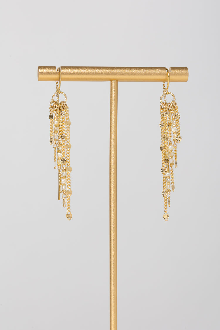 Slanted gold fringe threader earrings with pearl accents on a gold stand with light gray background 