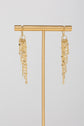 Slanted gold fringe threader earrings with pearl accents on a gold stand with light gray background 
