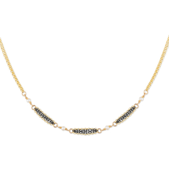Gold necklace with black and white bead details on a white background