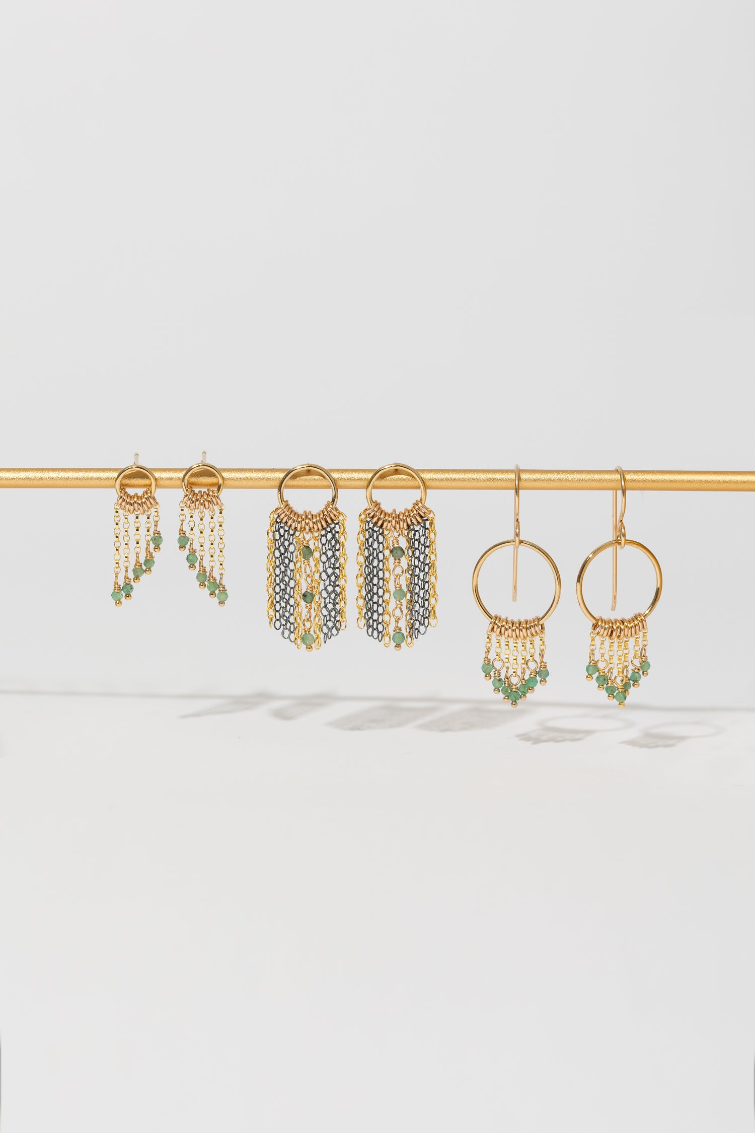 Three pairs of gold and mixed metal earrings with emerald bead accents on a gold bar