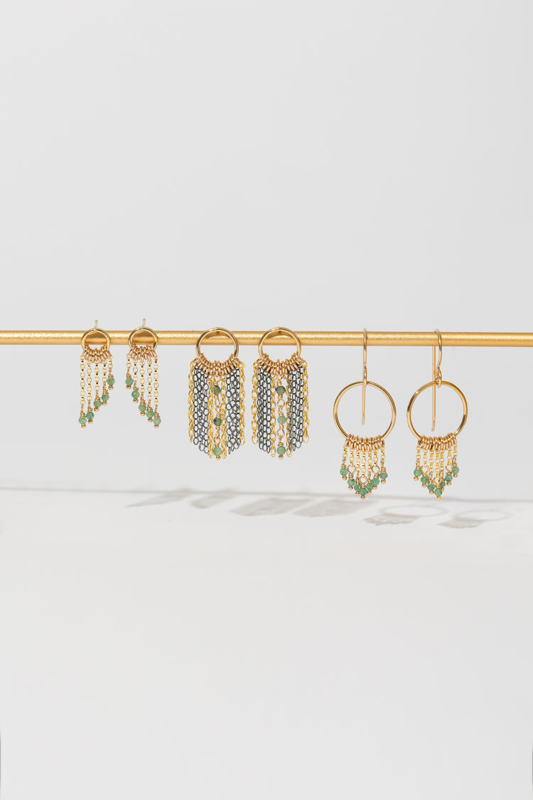 Three pairs of gold and mixed metal earrings with emerald bead accents on a gold bar