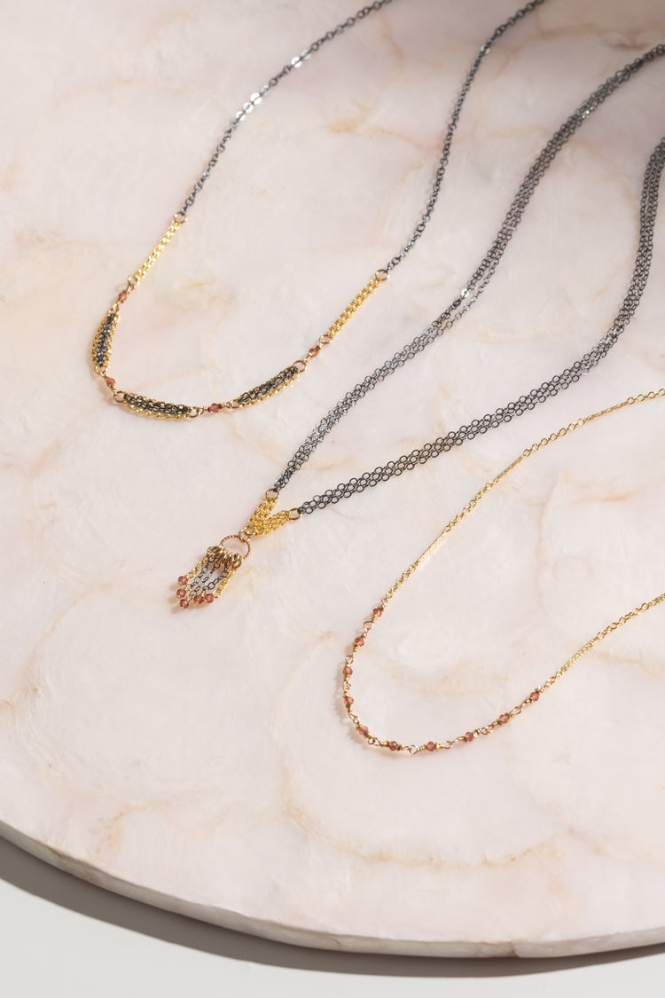 Three necklaces in gold and oxidized sterling silver and garnet stones on a marble surface