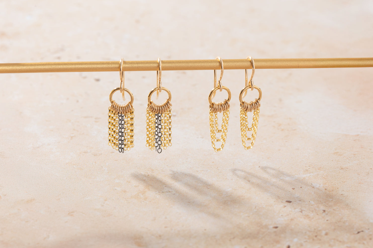 Gold chain earrings hanging on a rod against a neutral background
