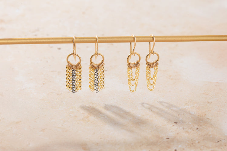 Gold chain earrings hanging on a rod against a neutral background
