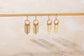 Gold chain earrings hanging on a rod against a neutral background