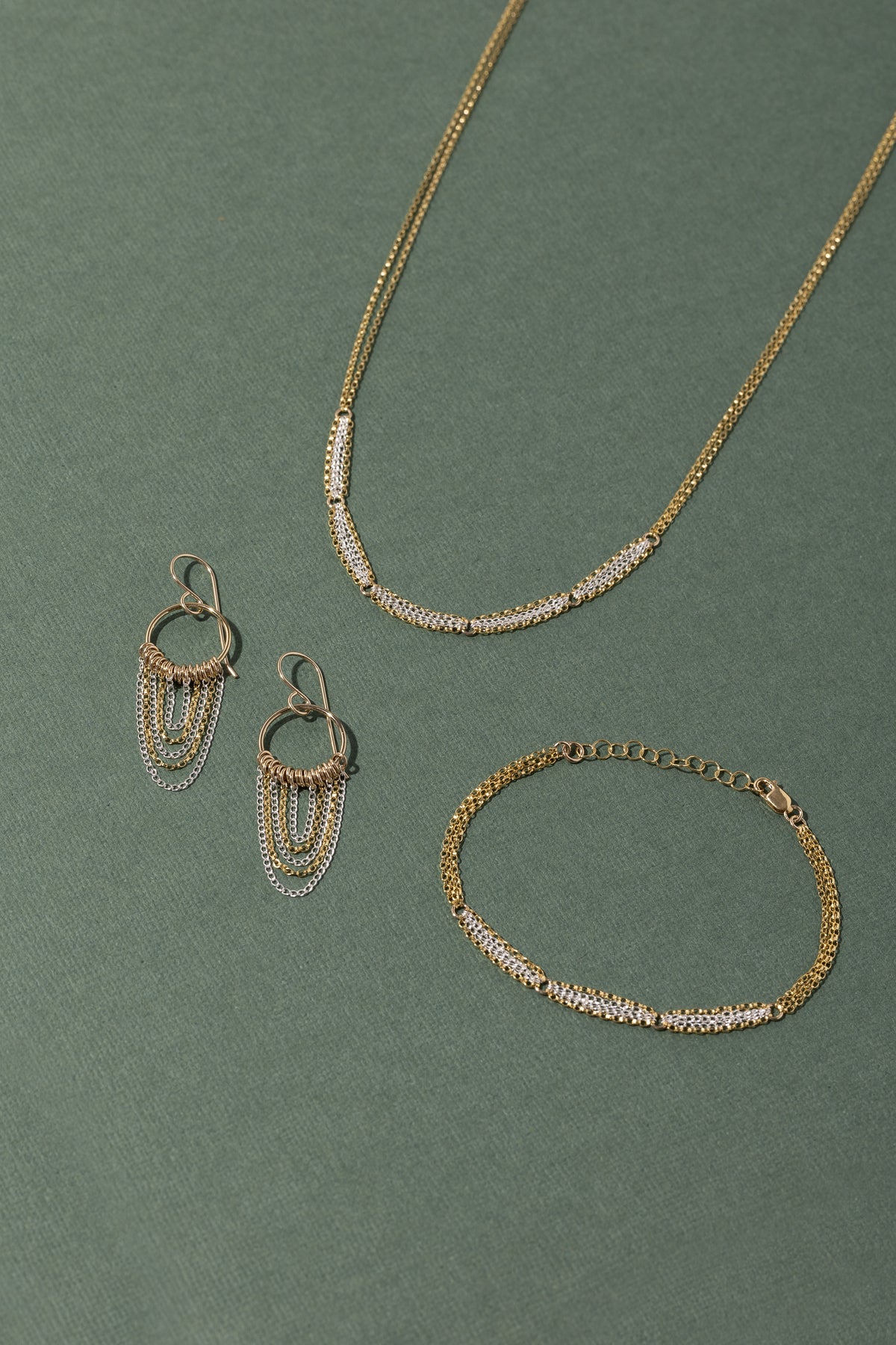 A pair of gold and silver earrings, necklace and bracelet on a green background