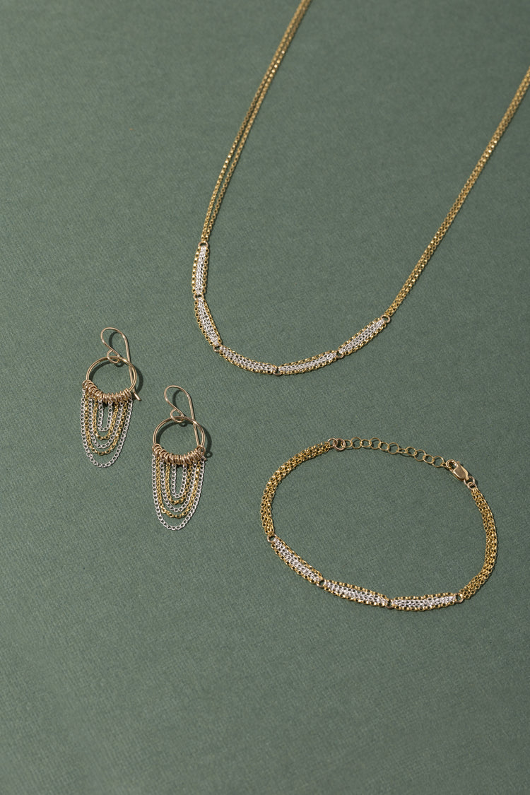 A pair of gold and silver earrings, necklace and bracelet on a green background