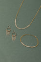 A pair of gold and silver earrings, necklace and bracelet on a green background