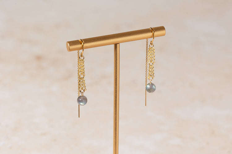 Gold earrings with labradorite drops on a gold stand against a beige background