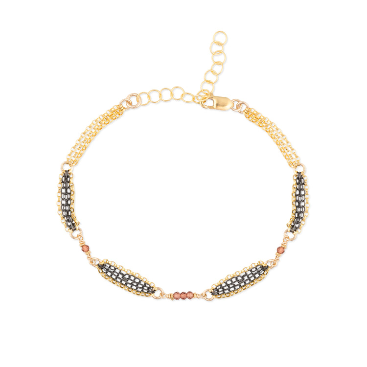 Gold bracelet with oxidized chain details and red garnet  beads on a white background
