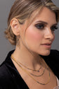 Model wearing mixed metal layering necklaces and earring with peacock pearl on a gray background