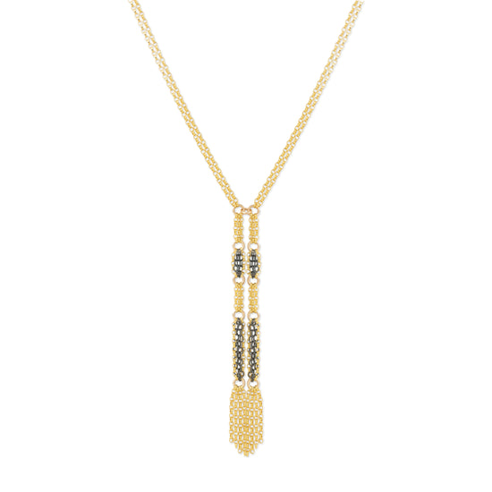 A gold-toned necklace with a long, intricate pendant featuring textured gold sections and small dark metallic accents, displayed against a solid white background.