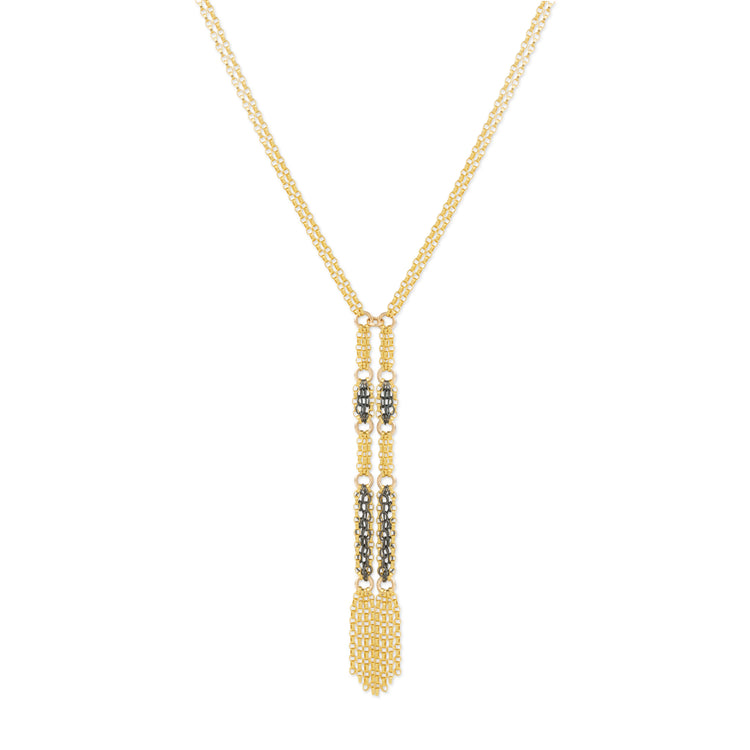 A gold-toned necklace with a long, intricate pendant featuring textured gold sections and small dark metallic accents, displayed against a solid white background.