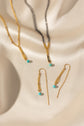 Gold-toned jewelry set including a necklace, matching drop earrings, and a chain bracelet arranged on draped cream satin fabric with turquoise bead accents.