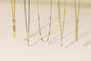 Five delicate gold-toned necklaces with mixed metallic and textured chain details, hanging against a warm cream background. Three of the necklaces feature small turquoise bead accents near the pendants.