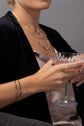 A model holds a drink and is wearing two mixed metal bracelets and layered necklaces in the background 
