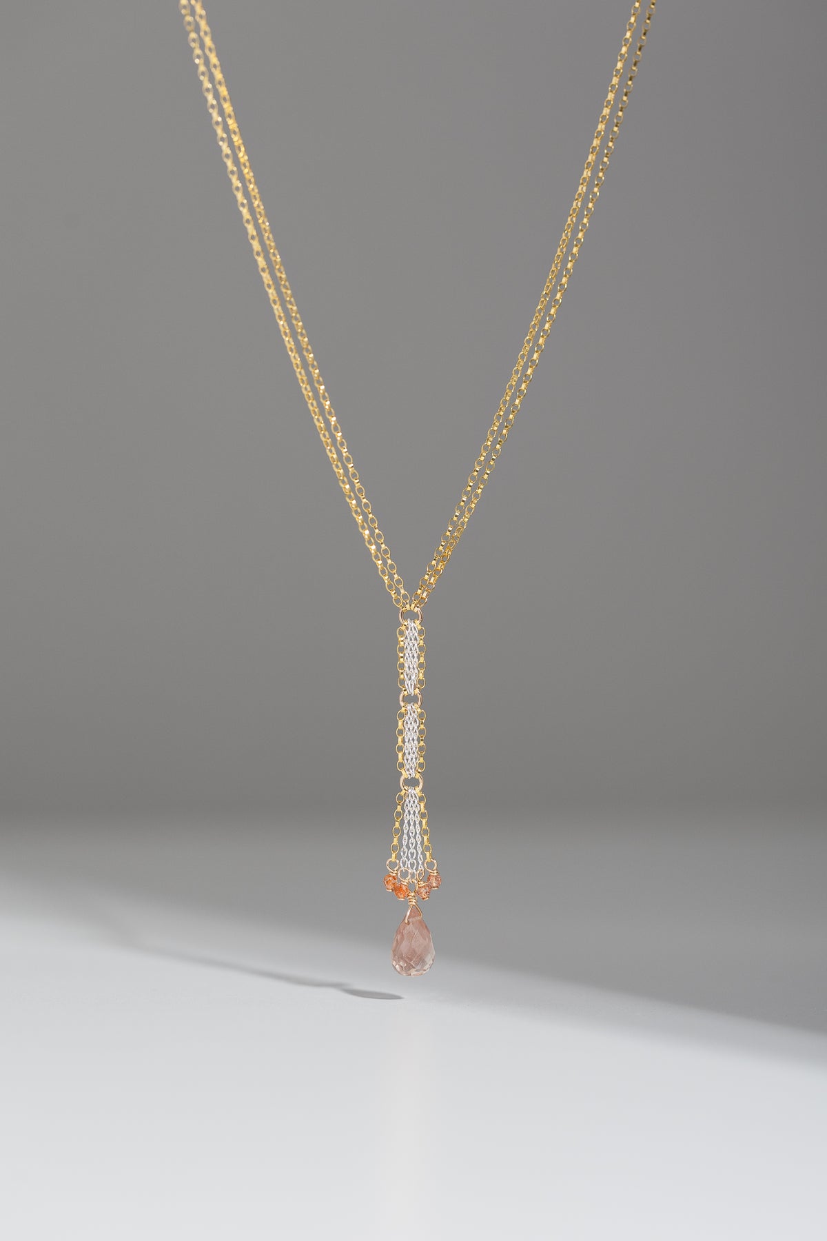 Mixed metal Y necklace with sunstone drop and accent beads hanging on a gray backgroud