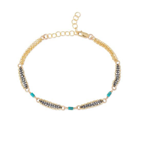 A gold chain bracelet featuring three horizontal rows of oxidized silver chain, accented with turquoise blue beads, displayed on a clean white background.