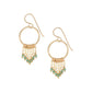 A pair of gold-colored circular earrings with intricate patterns and small emerald-colored gemstones.