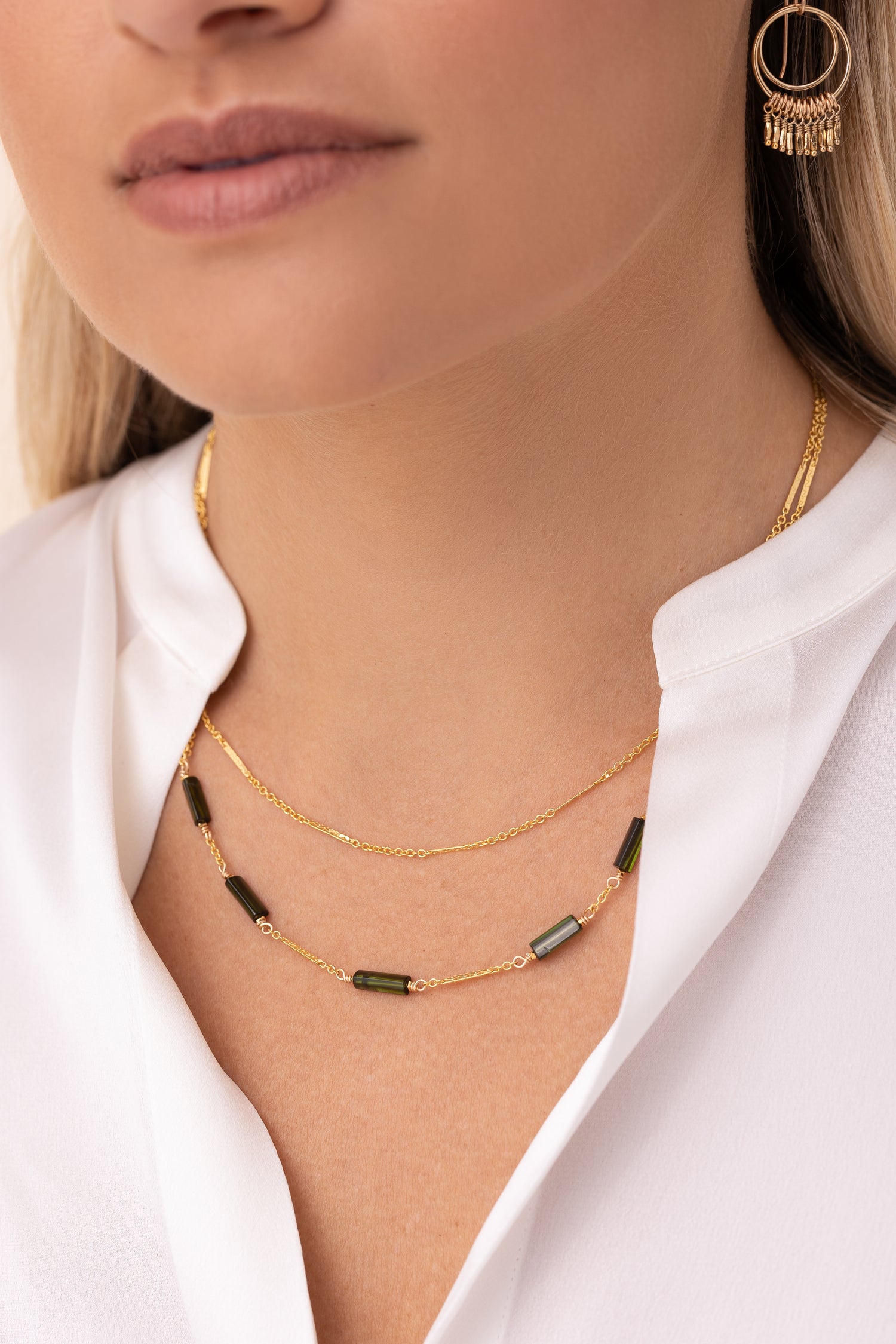 A model wearing a white shirt paired with the Linda double-stranded gold bar and link chain necklace featuring green tourmaline stones.