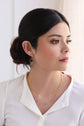 A model wearing a white shirt looking out a window while wearing the Aria petite gold fringe earrings and the Linda blue tourmaline necklace.